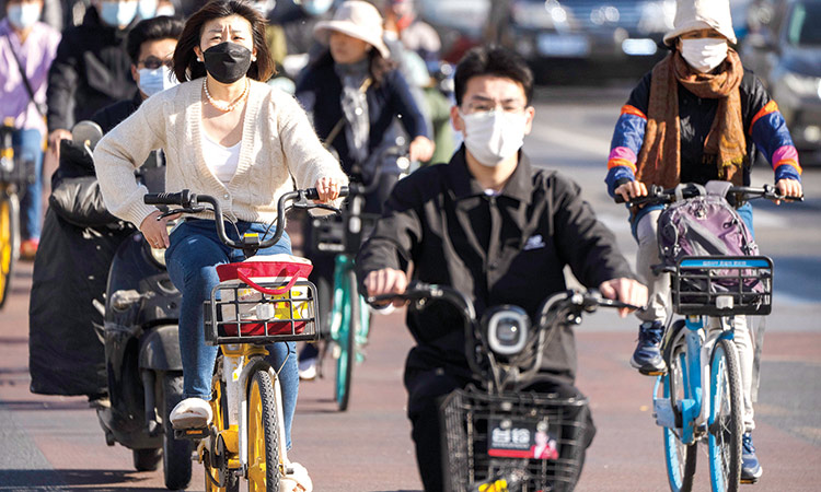 Commuters wearing face masks pedal bicycles cross an intersection in Beijing on Friday. Associated Press