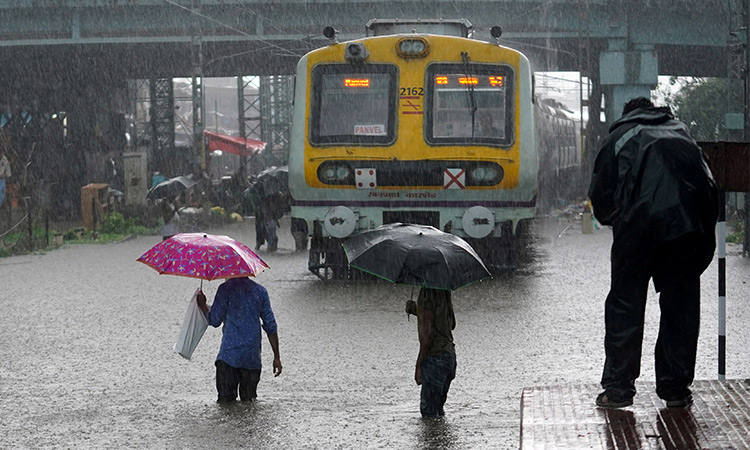 People cross inundated railway tracks next to a parked passenger train during heavy monsoon rains in Mumbai, India. File/Reuters