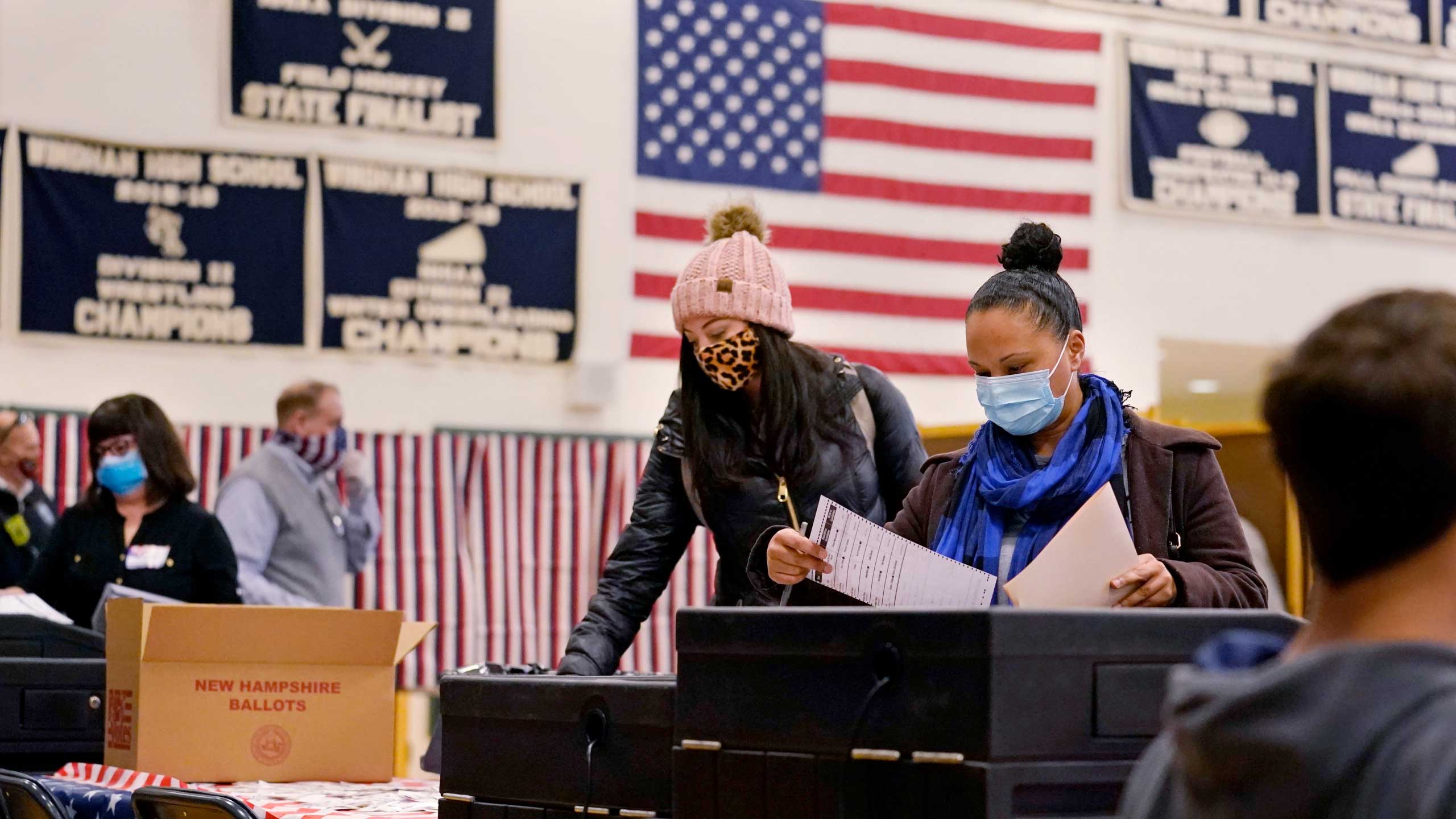 Two women, wearing protective masks due to the COVID-19 pandemic, cast their ballots at a polling station in Windham, New Hampshire. 