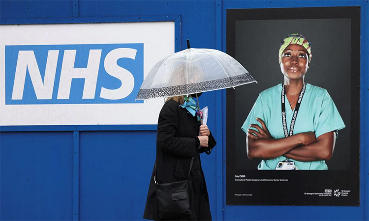 A person walks past an image of a National Health Service (NHS) worker displayed on hoardings outside a temporary field hospital at St George's Hospital in London. Reuters