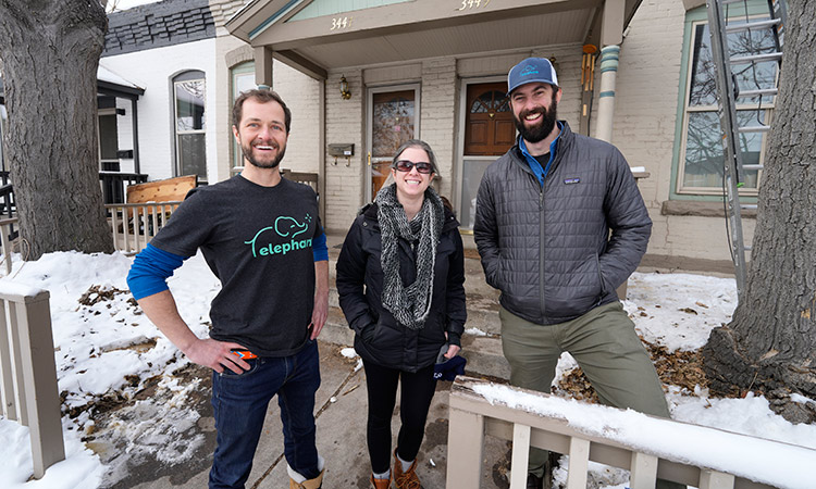 Homeowner Emily Kelly-Fischer, center, poses for a photo with David Richardson (left) and Rob Bayless of Elephant Energy outside her rowhouse where a heat pump is being installed, in northwest Denver. Associated Press
