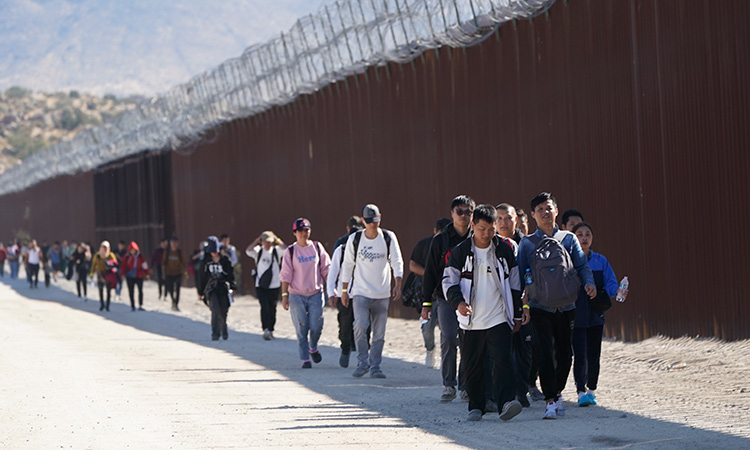 A group of people, including many from China, walk along the wall after crossing the border with Mexico to seek asylum, near Jacumba, California. AP